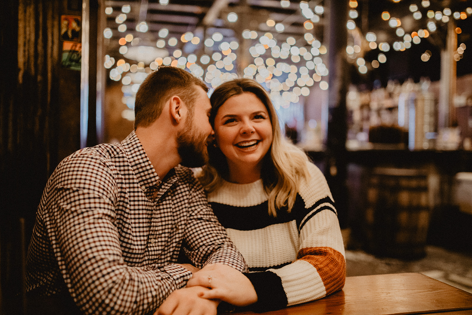couple sitting in coffee shop with string lights behind laughing during downtown chicago engagement photo