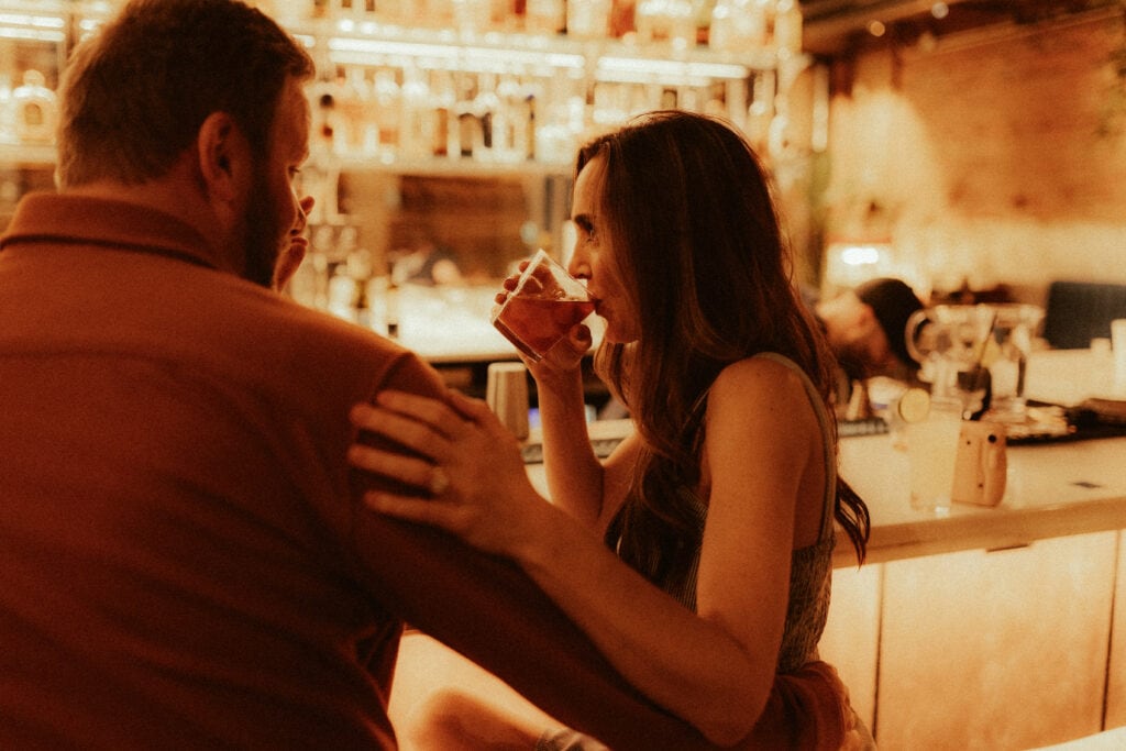 engagement photo of couple sitting at bar laughing during cocktails