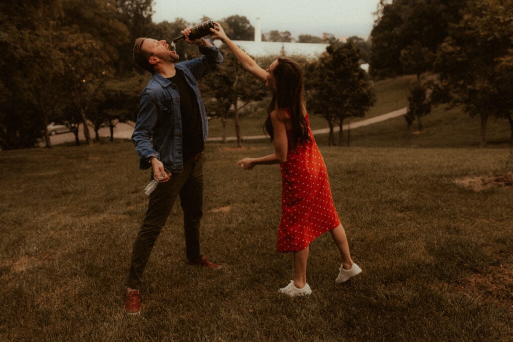 candid champagne engagement photo of girl pouring a bottle of champagne into fiances mouth