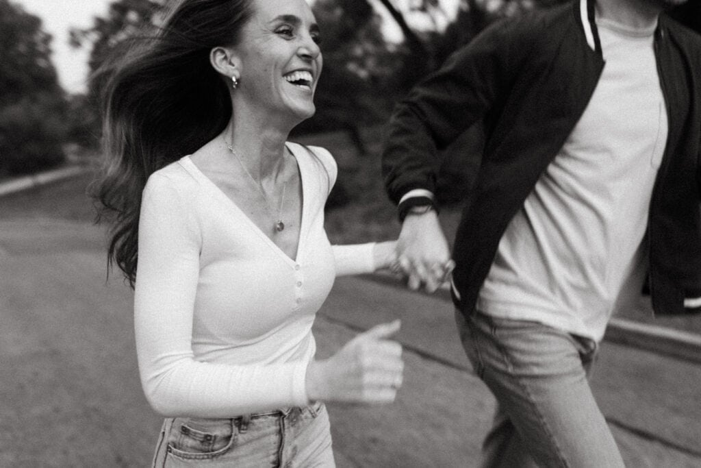candid black and white engagement photo of couple running hand in hand through cincinnati park