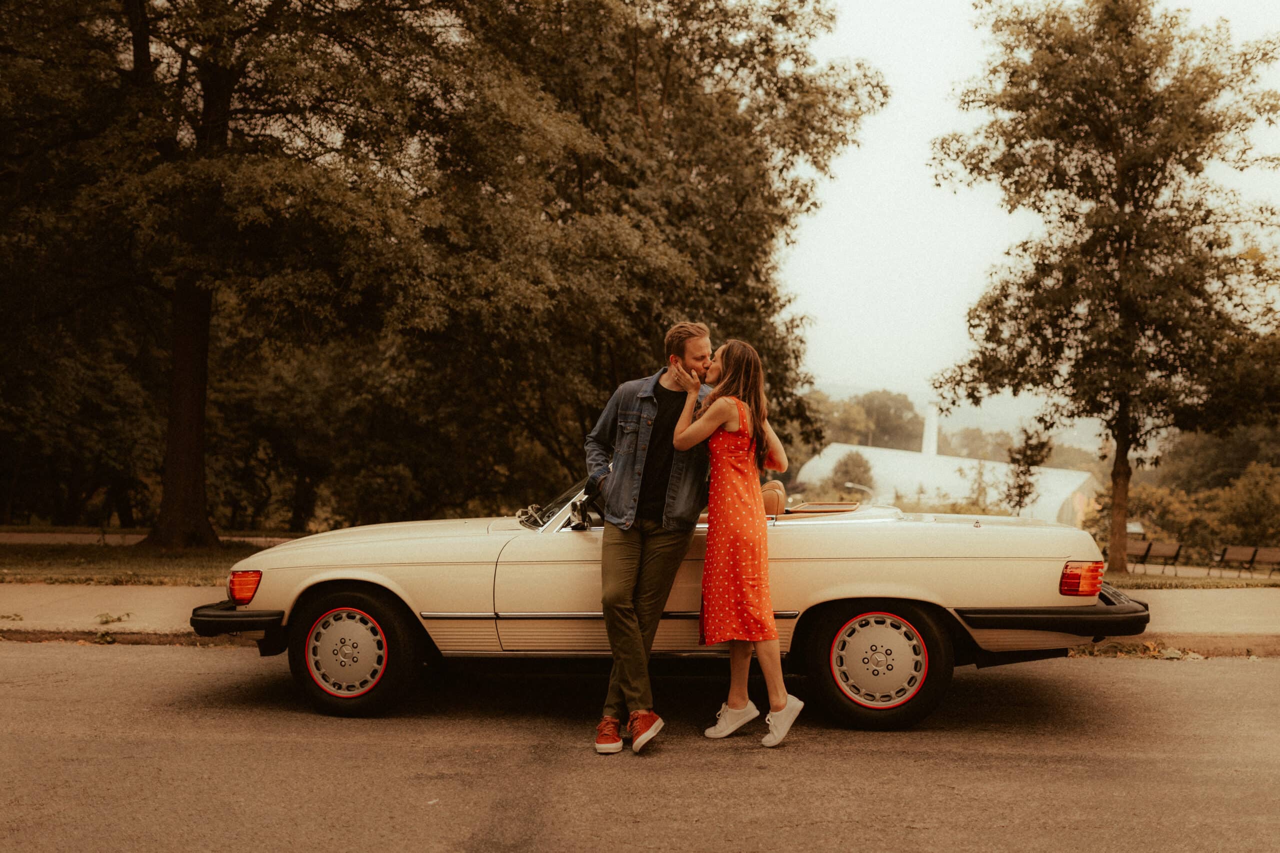 couple kissing in front of 1980s cream colored mercedes for retro engagement photo session