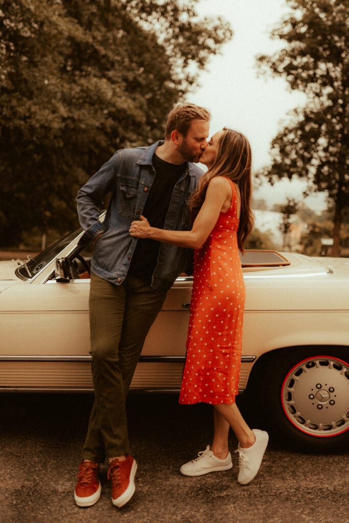 couple wearing retro outfits and kissing in front of 1980s mercedes for retro engagement photos