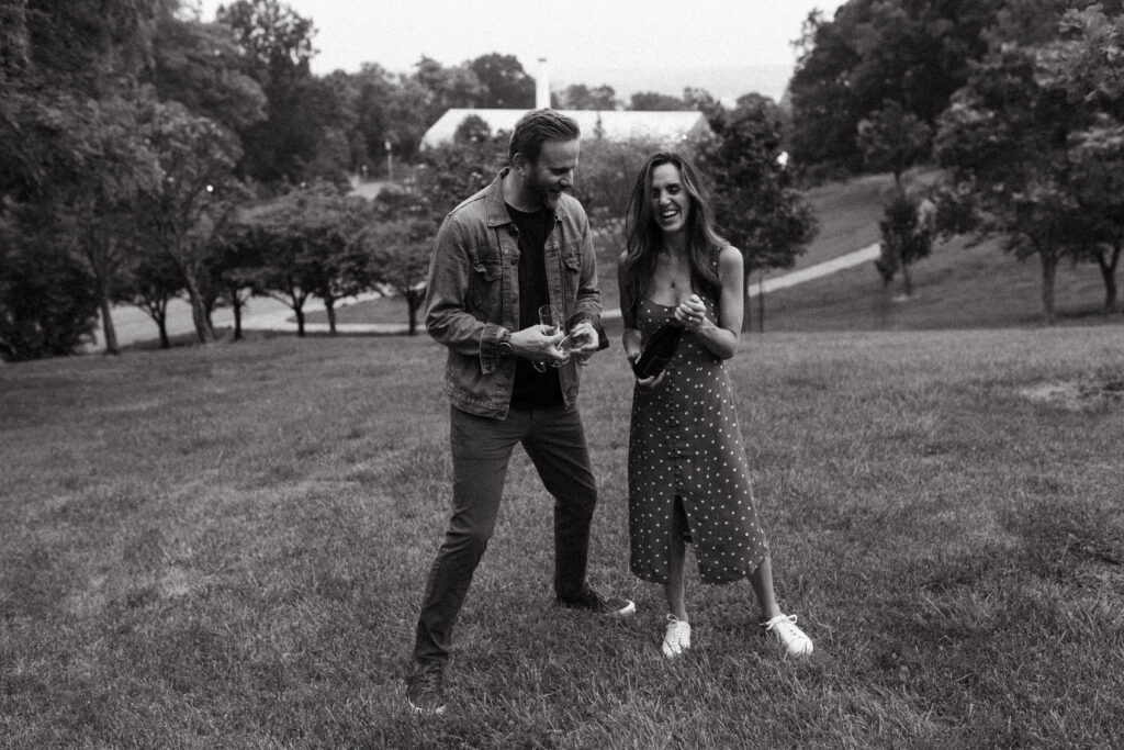 black and white engagement photo of couple popping a bottle of champagne