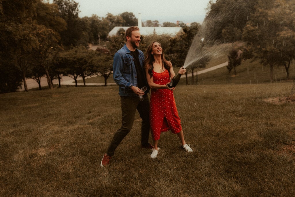 candid engagement photo of couple popping a bottle of champagne